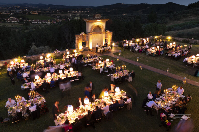 Evening dinner on the lawn with lamp-lit tables in front of the illuminated nymphaeum, Villa Il Cerretino