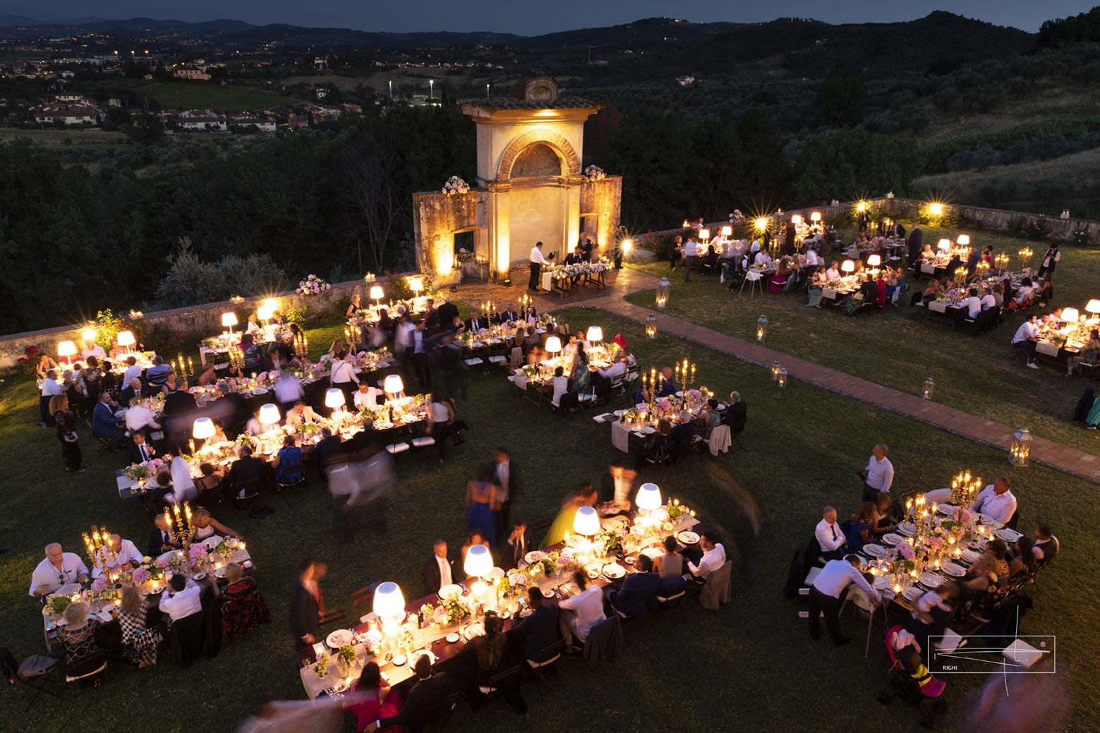 Evening dinner on the lawn with lamp-lit tables in front of the illuminated nymphaeum at Villa Il Cerretino