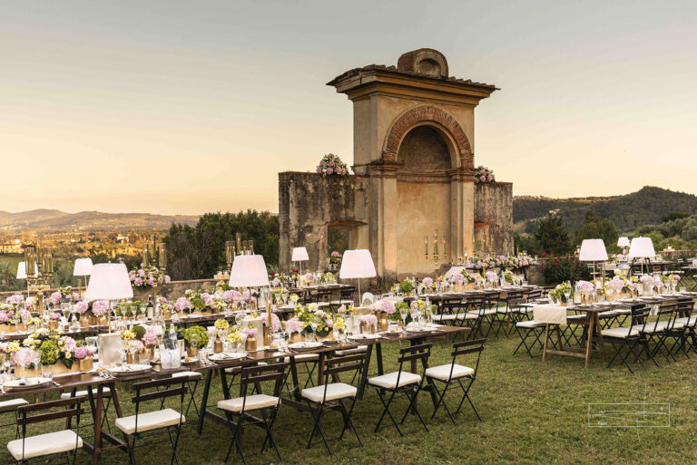 Long tables with lampshades and flowers set on the lawn before the historic nymphaeum at sunset, Villa Il Cerretino