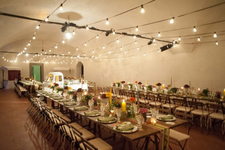 Long indoor tables with colourful flowers and candles under strings of lights in a vaulted hall, Villa Il Cerretino