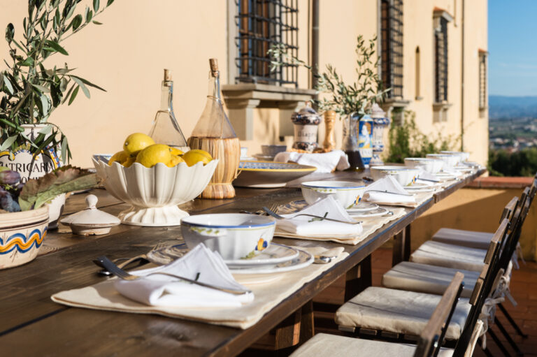 Long outdoor table on the terrace laid with lemons, ceramics and wine flasks beside the villa wall, Villa Il Cerretino