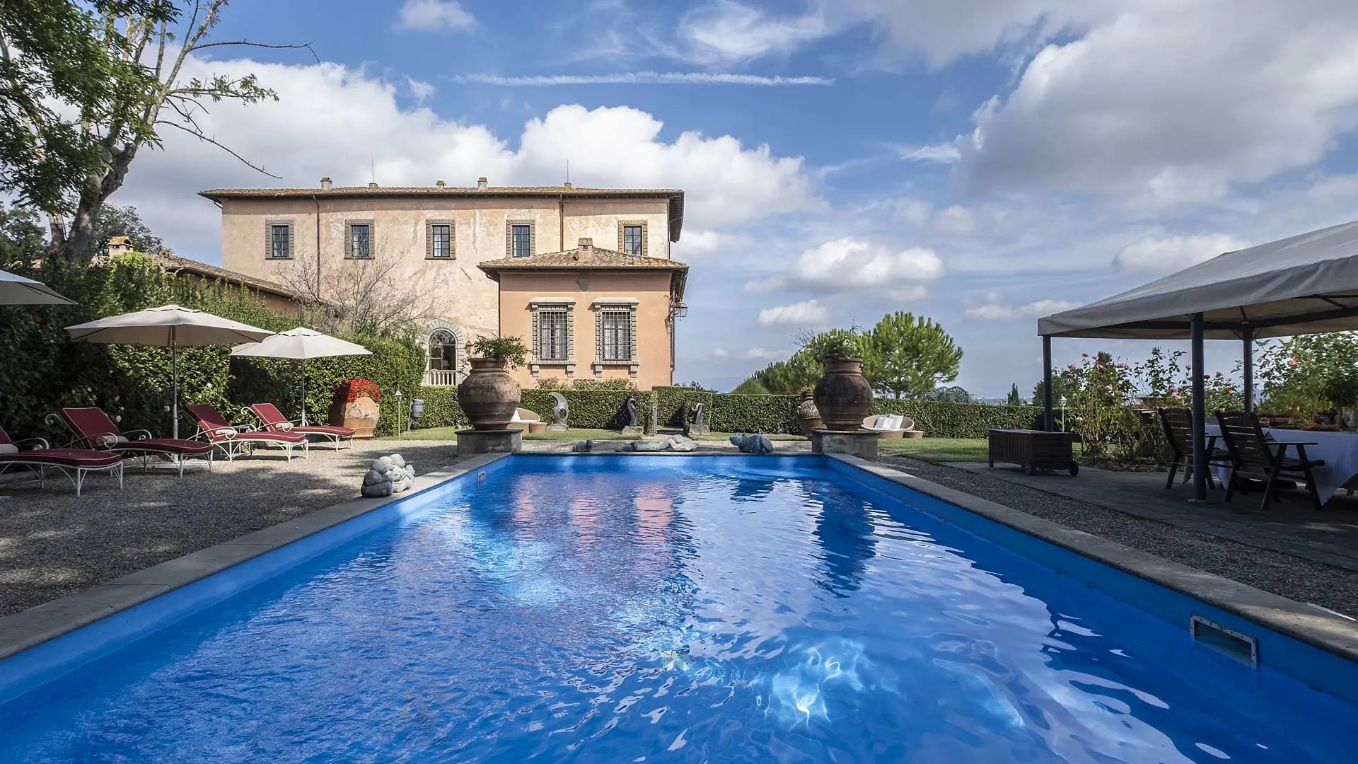 Outdoor pool with red loungers and a villa beyond at Villa Mangiacane