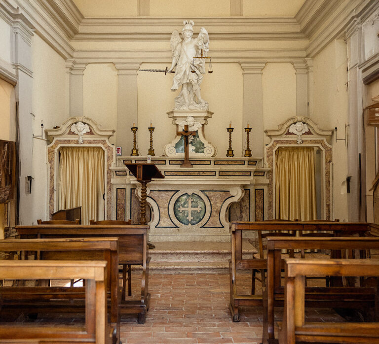 Inside the church: wooden pews, a marble altar and a statue of the archangel above, Villa Ormaneto