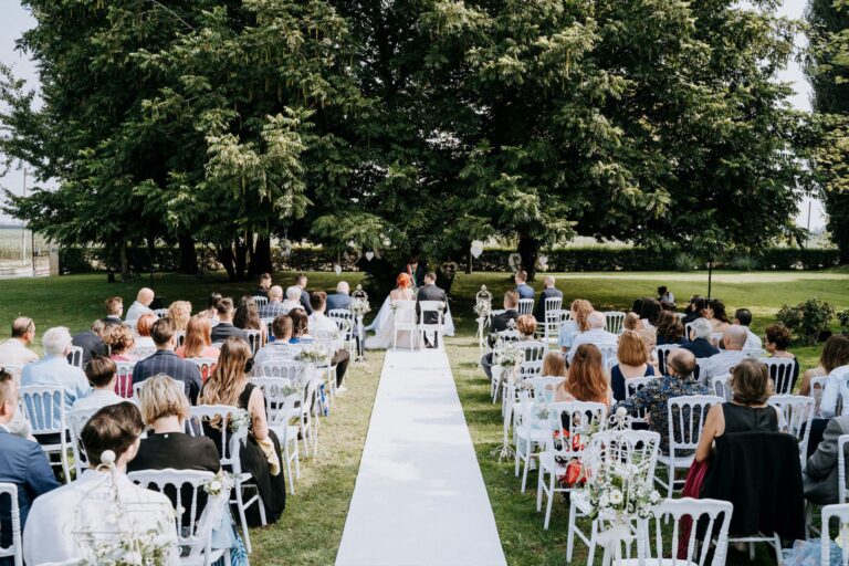 Guests seated either side of a white aisle for an outdoor ceremony in the park, Villa Ormaneto
