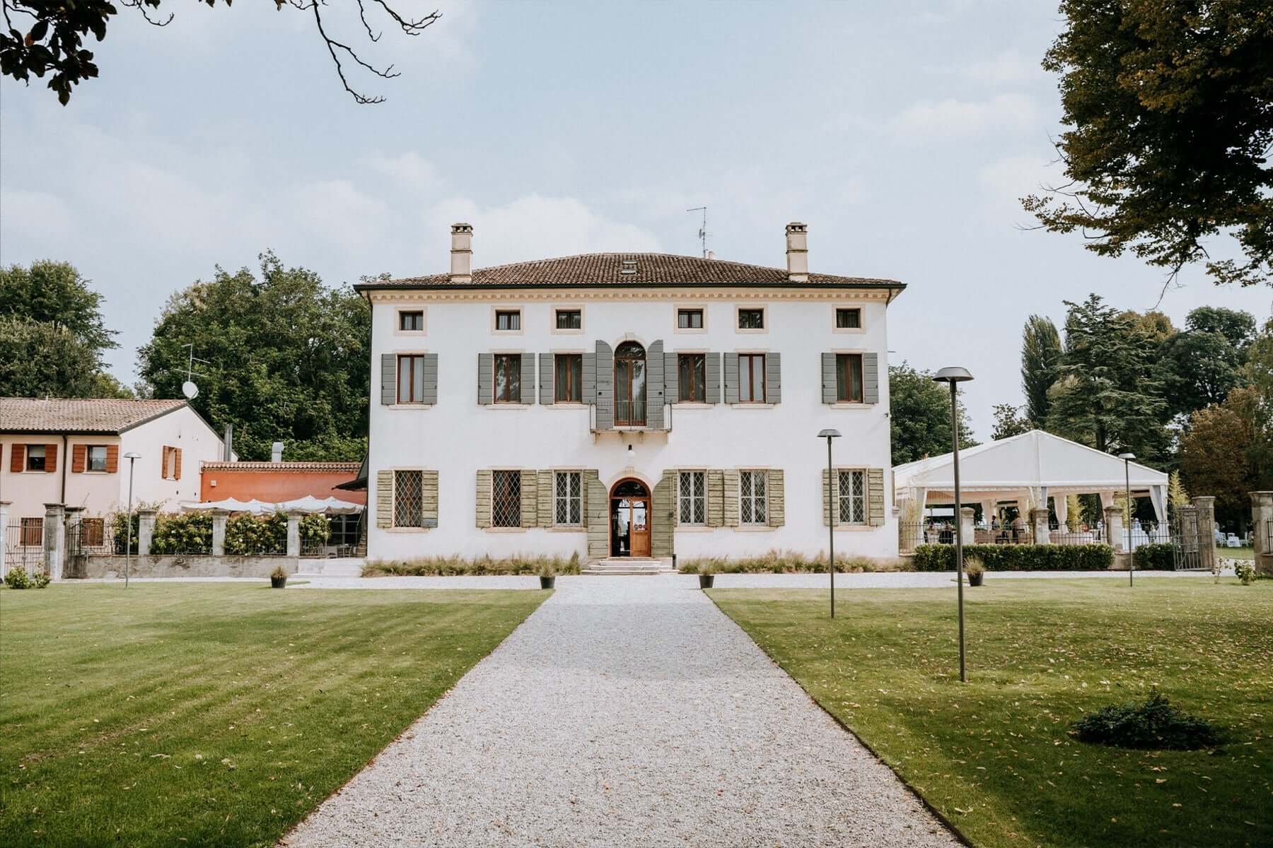 The villa's pale facade and green shutters at the end of the gravel avenue across the lawn, Villa Ormaneto