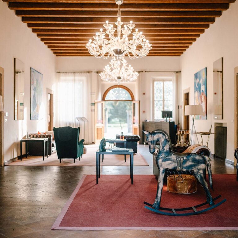 The main salon of the villa, with a beamed ceiling, glass chandeliers and a rocking horse, Villa Ormaneto