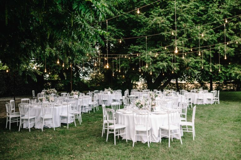 Round tables laid in white under strings of lights among the park's trees, Villa Ormaneto