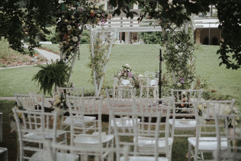 Garden ceremony set up with white chairs and a floral arch under the trees, Villa Sofia