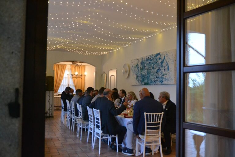 A long lunch table under strings of lights in the same main room, seen through the open doors, Villa Sofia