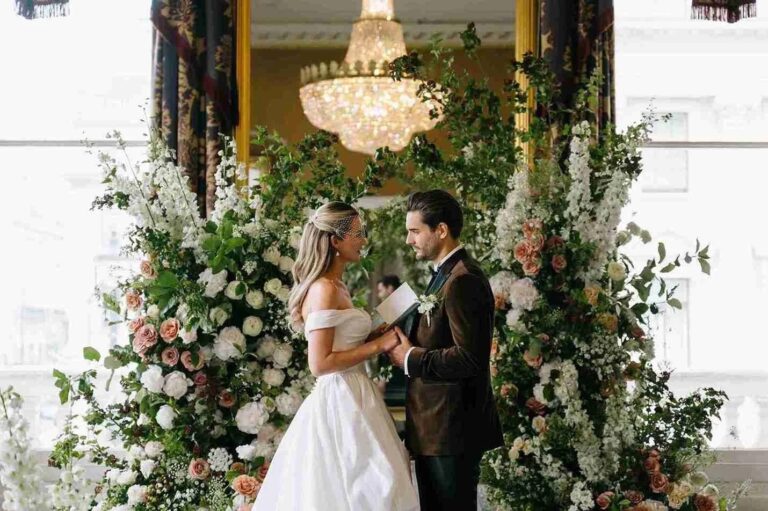 The couple beneath a floral arch and chandelier after the ceremony, 116 Pall Mall