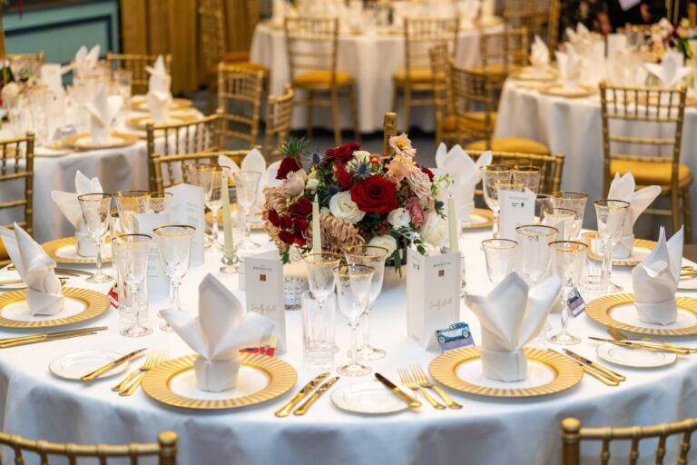 A banqueting table setting, napkin fans, gold chargers and red and white florals, 116 Pall Mall