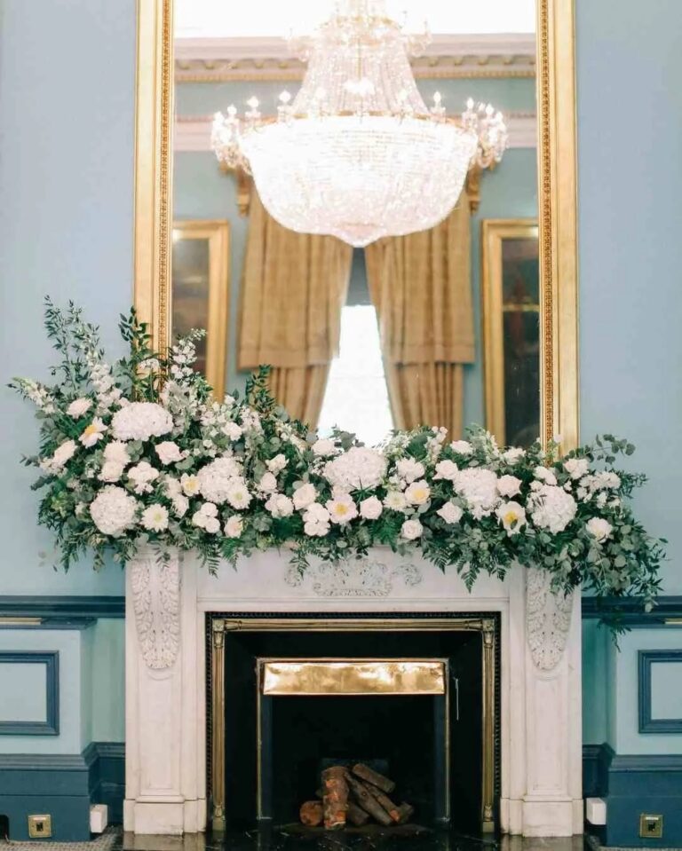 A white and green floral installation across a marble chimneypiece, 116 Pall Mall