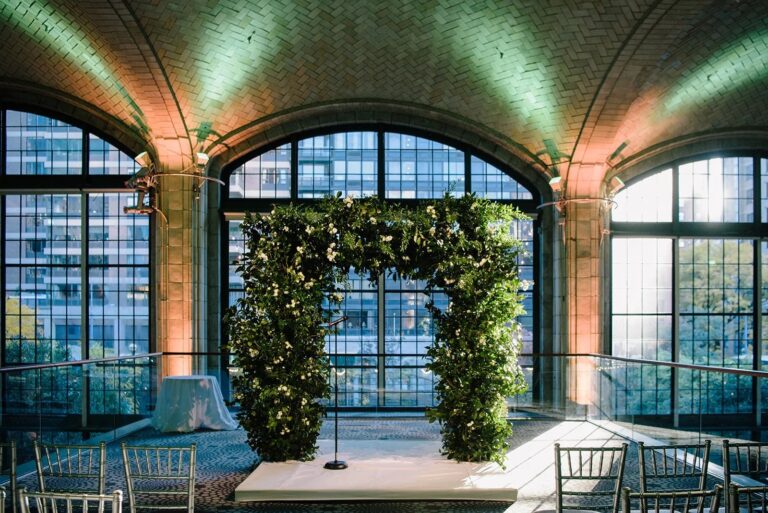 Ivy and white-flower ceremony arch before a tall arched window at Gustavino's, New York, 5th Avenue Weddings