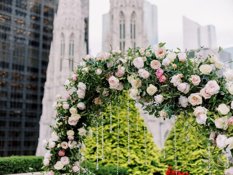 Rose and greenery ceremony arch on a Manhattan terrace with the cathedral spires behind, 5th Avenue Weddings