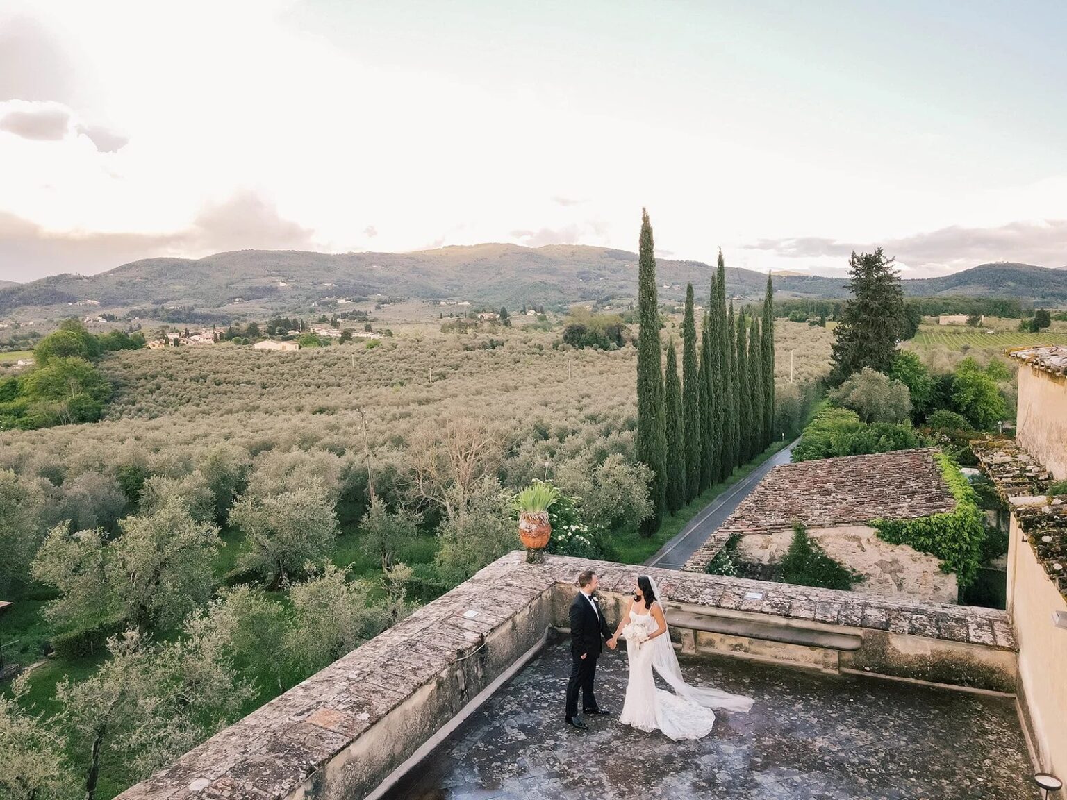 A couple on a stone terrace above olive groves and cypress trees in Tuscany