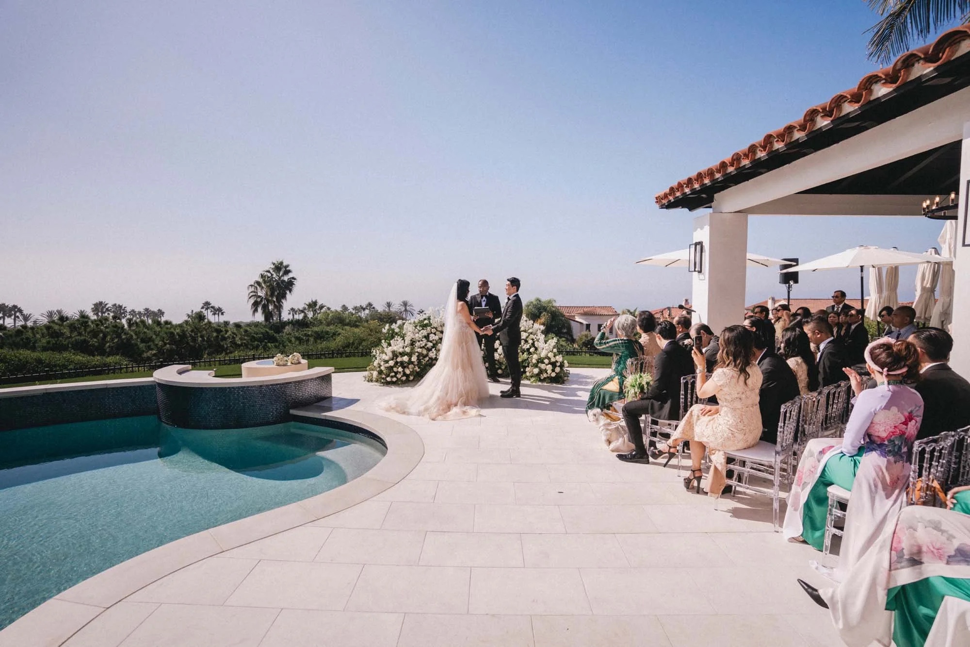 Couple and guests at a ceremony on a pool terrace overlooking the coast, About Details Details