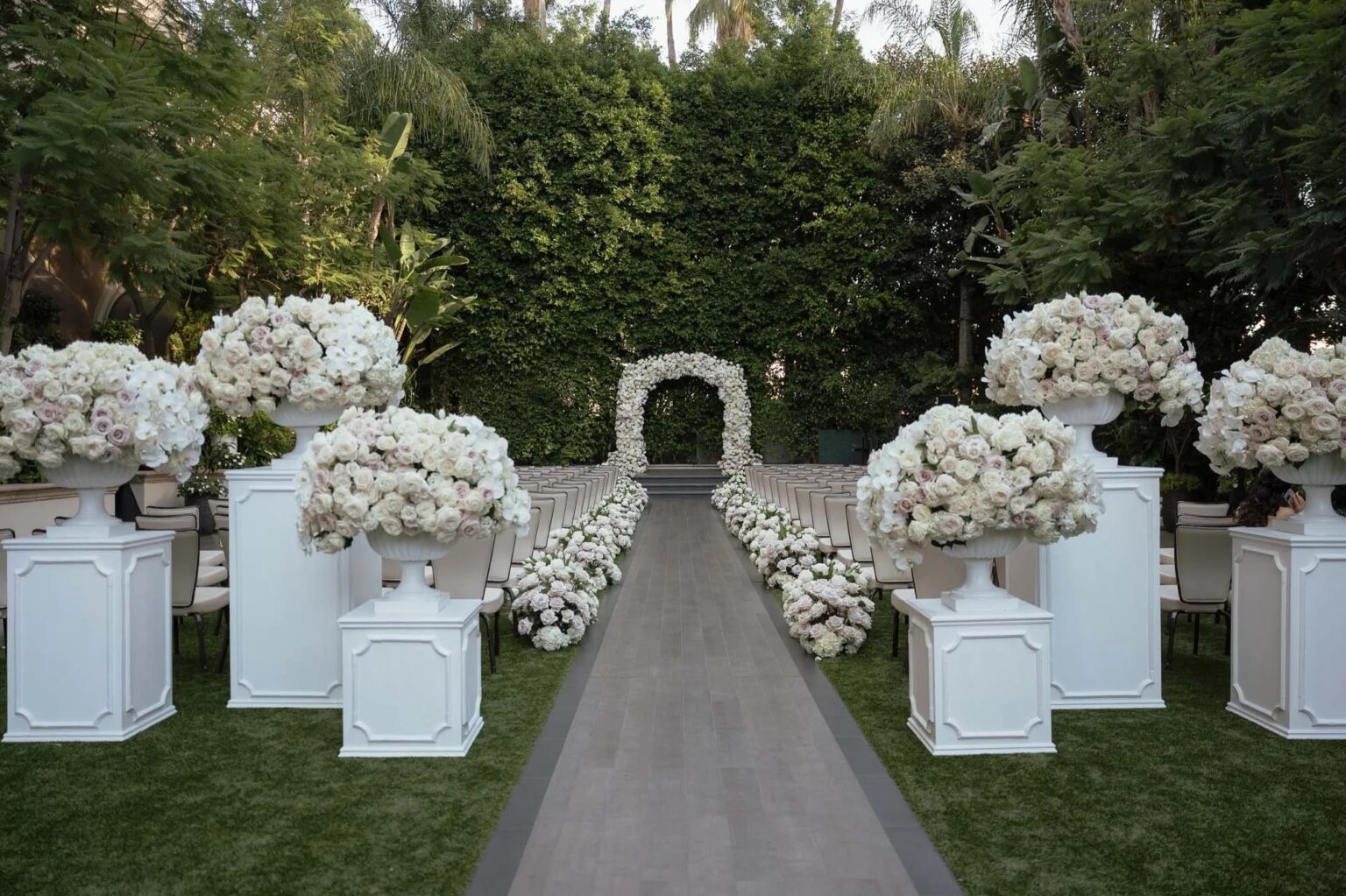 A lawn aisle lined with white pedestals topped with hydrangeas and roses