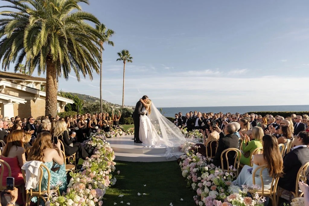 A couple at the end of a floral aisle on a white platform by the sea