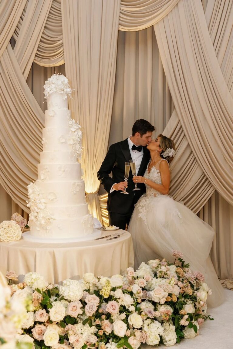 Couple with a tall white wedding cake in front of cream drapery, About Details Details