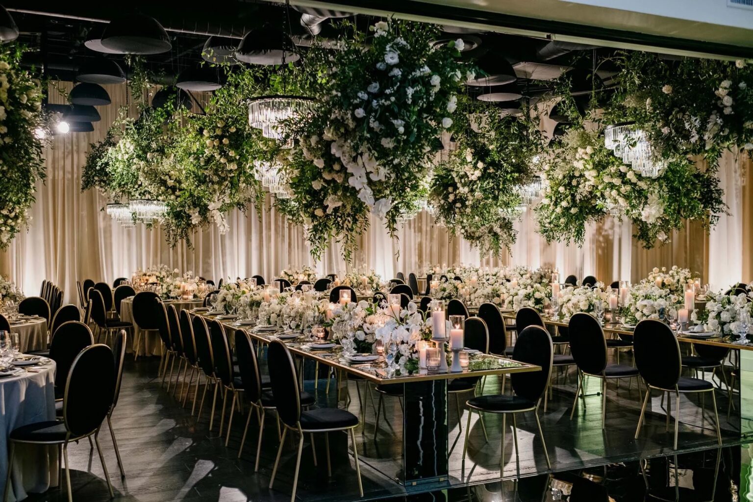 Long reception tables beneath hanging greenery and white flowers, with candles