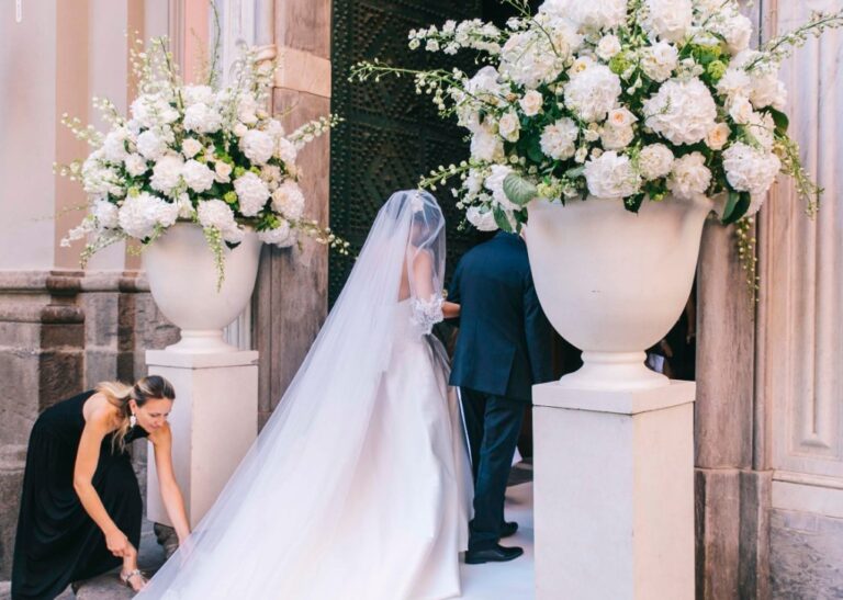 Bride in a long veil at the church door between white floral urns, Villa Fattorusso, Alba Greco