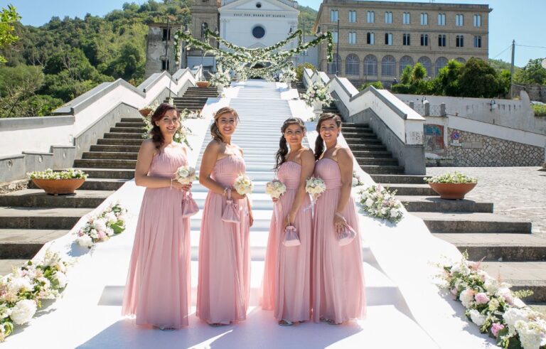 Bridesmaids in pink on a white-carpeted stone staircase lined with flowers, Alba Greco