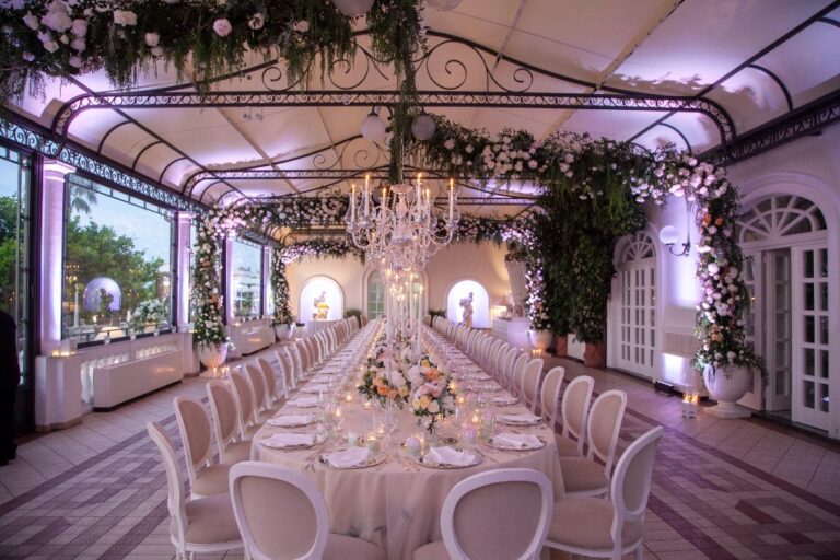 Pink-lit glasshouse reception with a long table and floral installations in Campania, Alba Greco