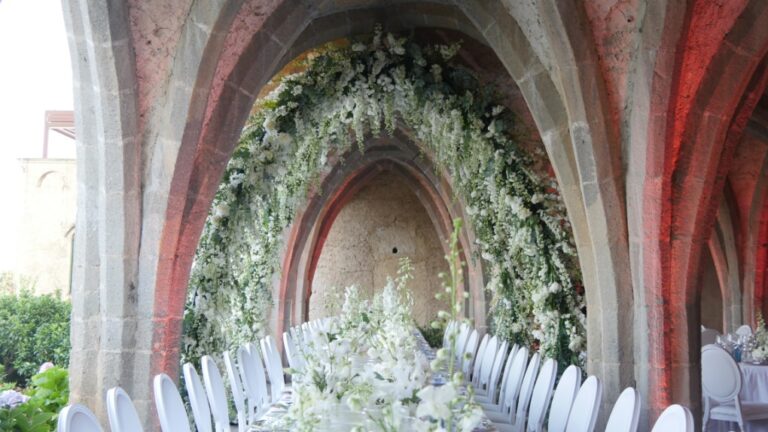 Long table beneath a vaulted stone arcade dressed with hanging greenery in Ravello, Alba Greco