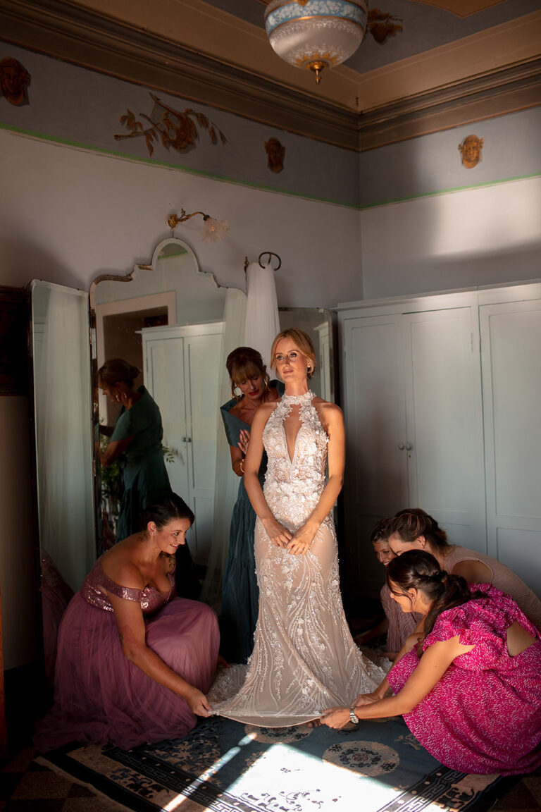 Bride dressed in a frescoed bedroom while her bridesmaids help, Alessandro Mari Photography
