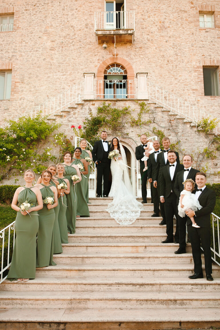 Wedding party on a grand stone staircase beneath a brick facade, Alessandro Mari Photography