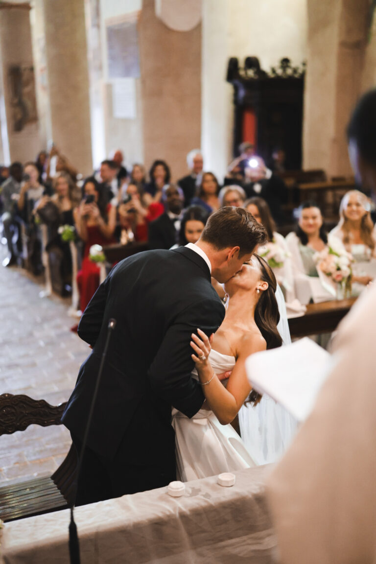 Groom kissing the bride in a church as guests watch, Alessandro Mari Photography