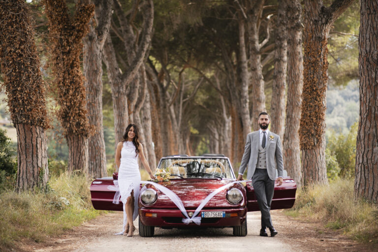 Couple beside a red vintage convertible along an avenue of umbrella pines, Alessandro Mari Photography