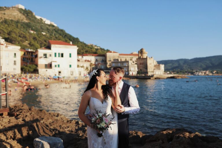 Couple by the sea with a harbour village behind, Alessandro Mari Photography