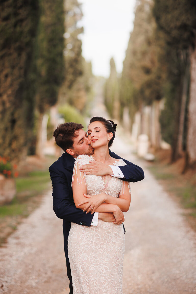 Couple embracing on a cypress-lined drive, Alessandro Mari Photography