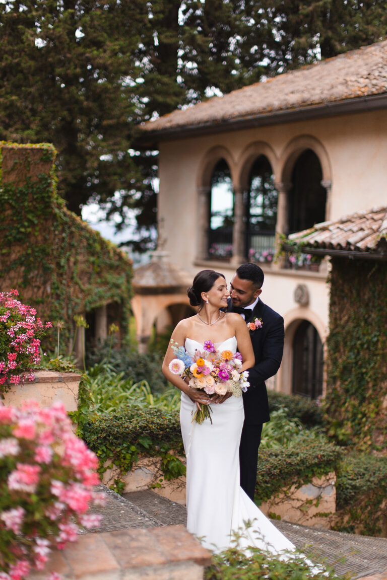 Couple with a colourful bouquet beside a loggia and flowering garden, Alessandro Mari Photography