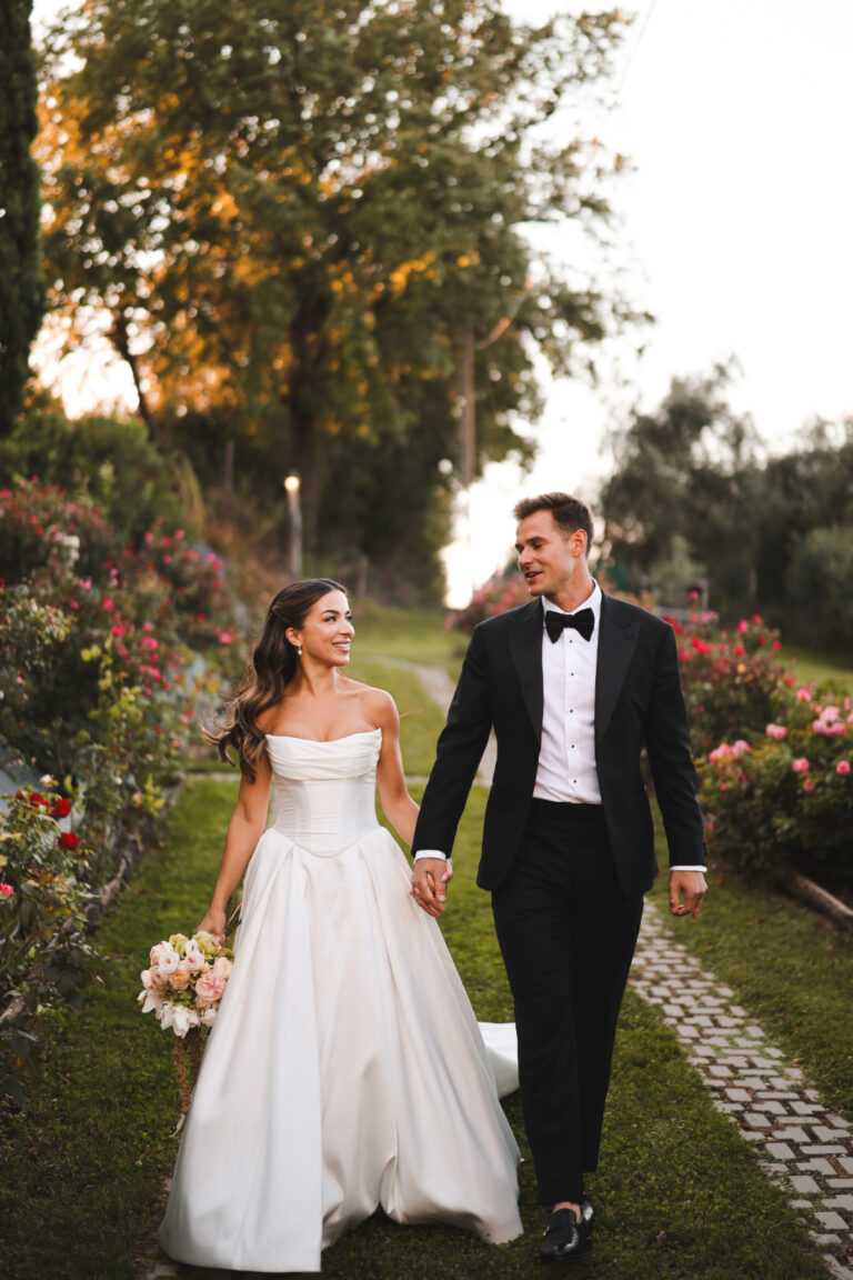 Couple walking hand in hand along a rose-lined path, Alessandro Mari Photography