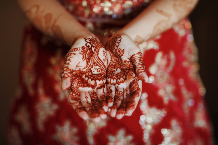 Henna-painted hands against a red embroidered dress, Alessandro Mari Photography