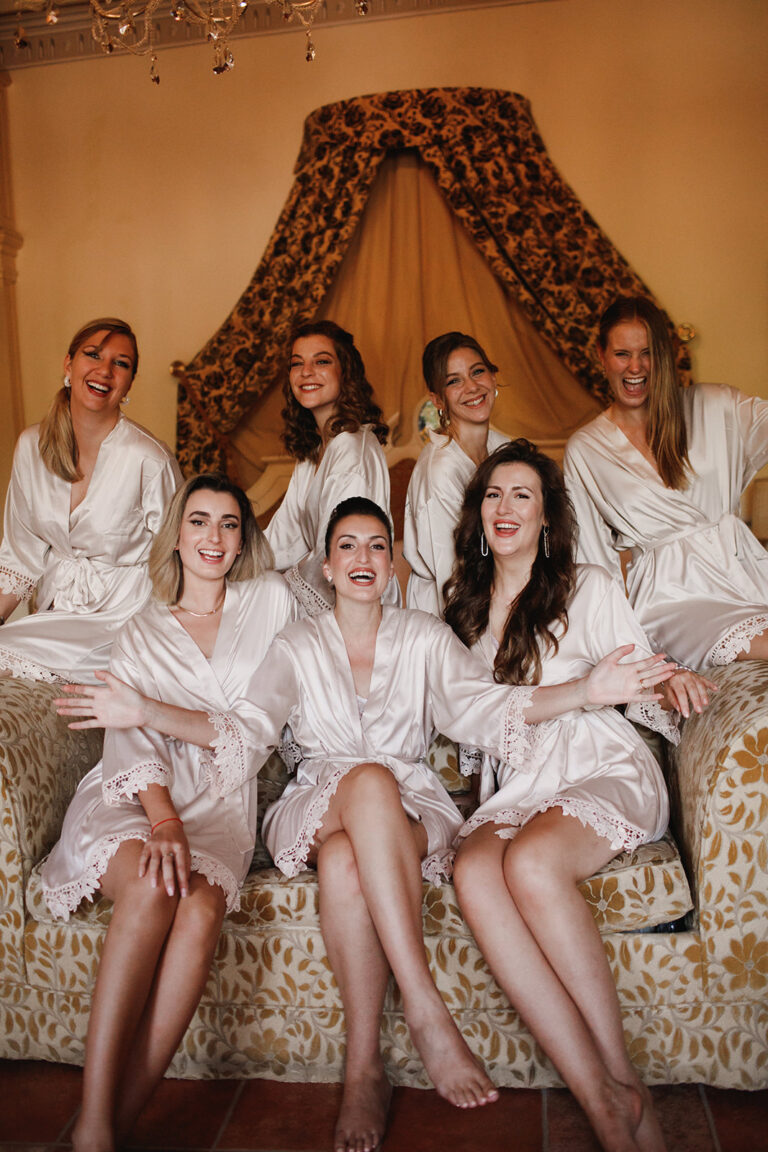 Bridesmaids in white robes laughing on a canopy bed, Alessandro Mari Photography