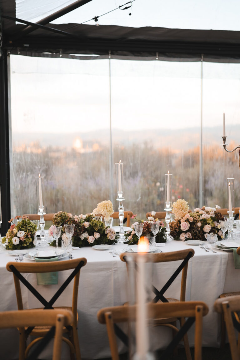 Dinner table set with candles in front of a glass wall at dusk, Alessandro Mari Photography