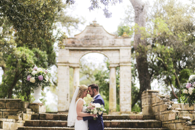 Couple at a stone garden arch with flower arrangements, Alessandro Mari Photography