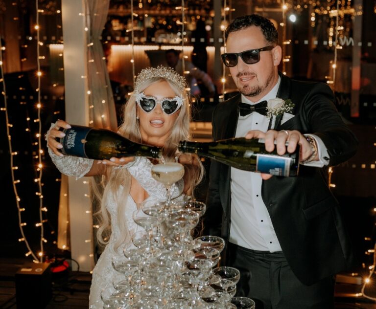 Couple pouring champagne over a glass tower under festoon lights, Algarve Wedding Planners