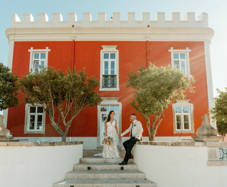 Couple seated on the steps of a red crenellated villa, Algarve Wedding Planners