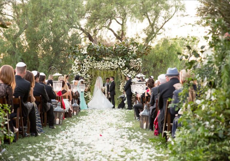 Garden ceremony with a petal-strewn aisle beneath trees and floral arch, Aliana Events