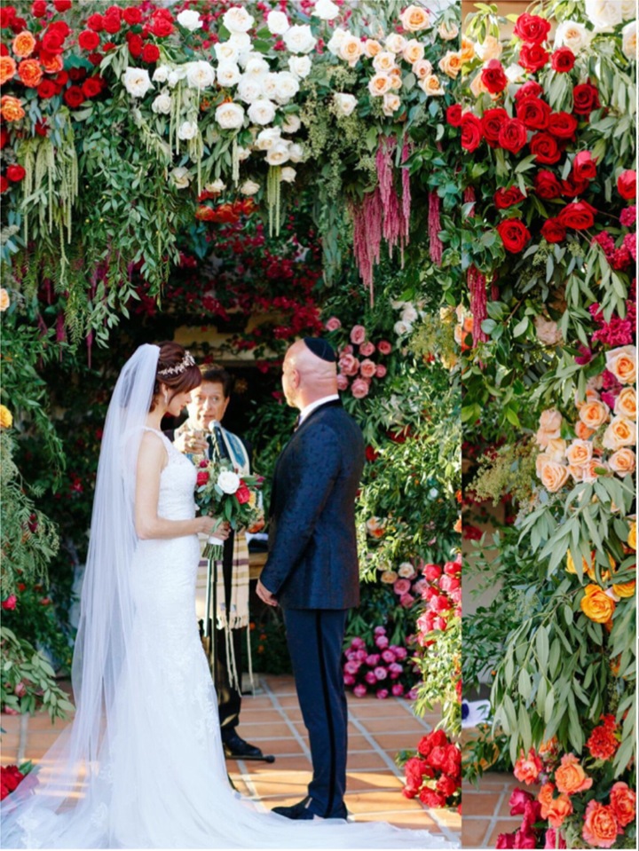 Ceremony beneath an arch of red, orange and white flowers, Aliana Events