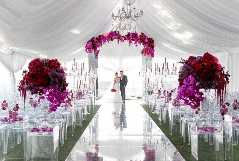 Ceremony aisle with a magenta floral arch and clear candelabra in a white draped tent, Aliana Events