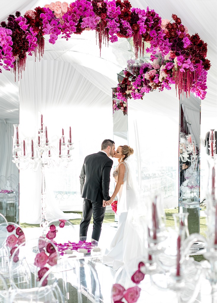 Couple under a magenta floral arch in a white tent, Aliana Events