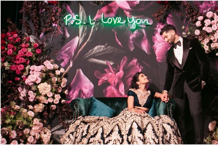 Couple seated in front of a floral wall with a neon sign, Aliana Events
