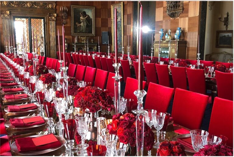 Long dinner table with red chairs and red roses in a historic hall, Aliana Events