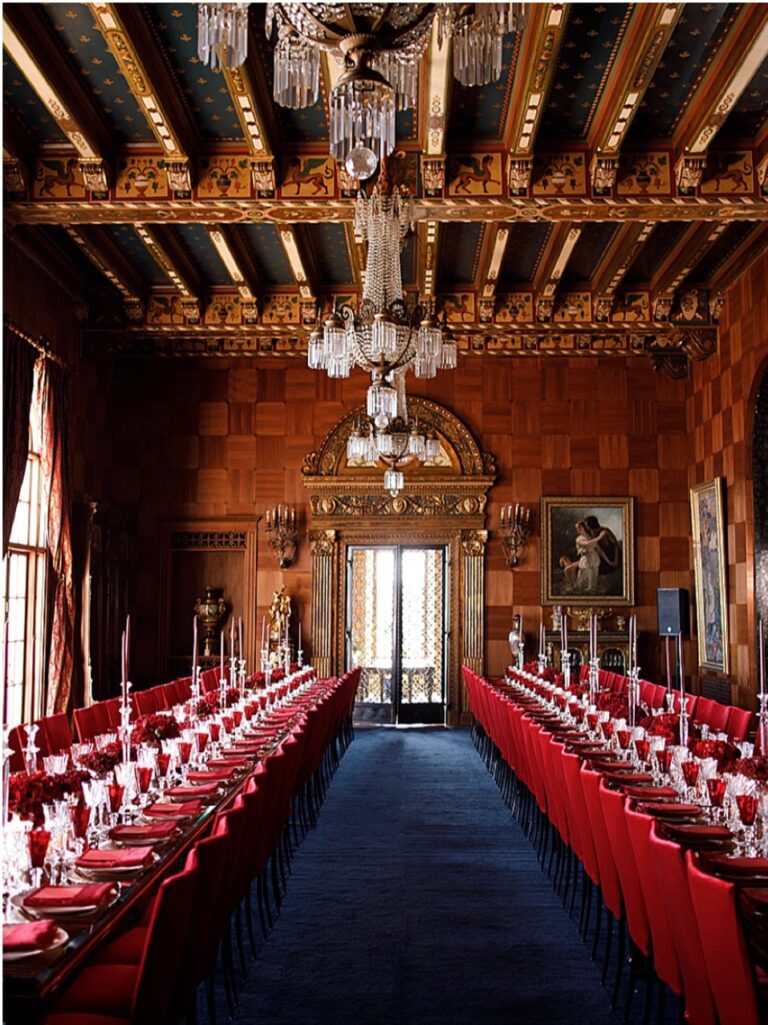 Historic hall with a coffered ceiling, chandeliers and red-draped dinner tables, Aliana Events