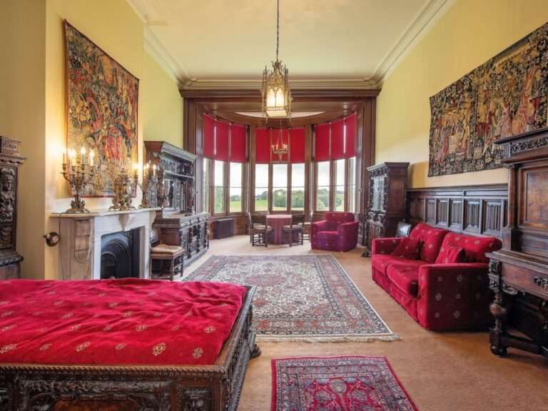 A long drawing room dressed in red, with tapestries, sofas and a chandelier, Allerton Castle